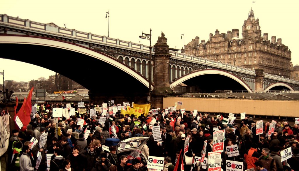 A crowd of people protesting against the backdrop of the North Bridge, Edinburgh